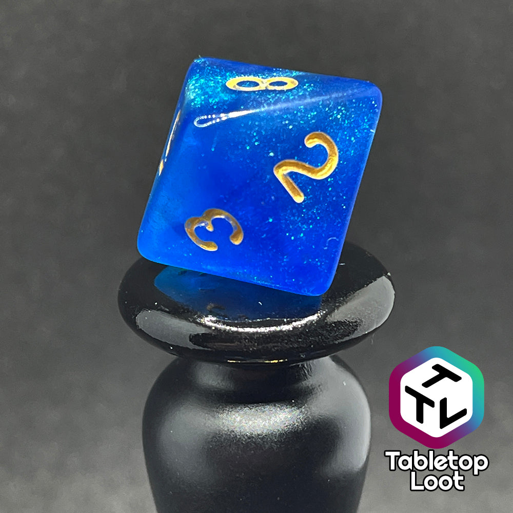 A close up of the D8 from the Air Genasi 7 piece dice set from Tabletop Loot with swirls of glittering tones of blue and gold numbers.