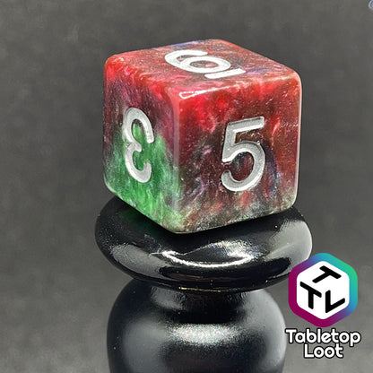 A close up of the D6 from the Changeling 7 piece dice set from Tabletop Loot with swirls of pearlescent red, green, and blue and silver numbering.