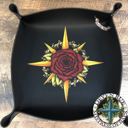A black dice tray has a rose motif compass rose by Deven Rue in the middle and snaps in the corners.