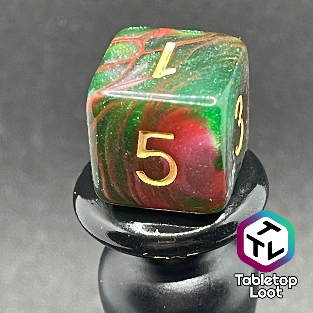 A close up of the D6 from the Enchanted Forest 7 piece dice set from Tabletop Loot with swirls of pink and green glittery resin and gold numbering.