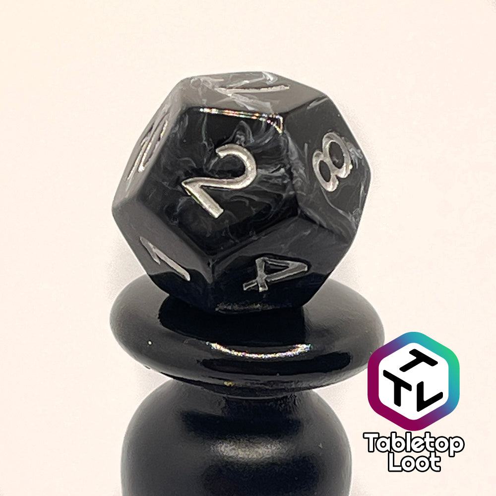 A close up of the D12 from the Form of Dread 7 piece dice set from Tabletop Loot with swirls of white in black resin and silver numbering.