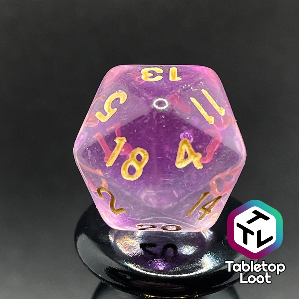 A close up of the D20 from the Incantation 7 piece dice set from Tabletop Loot with swirls of fuchsia in clear and gold numbering.