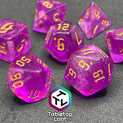 A close up of the Moxie 7 piece dice set from Tabletop Loot; fuchsia dice packed with glitter and gold gothic numbering.