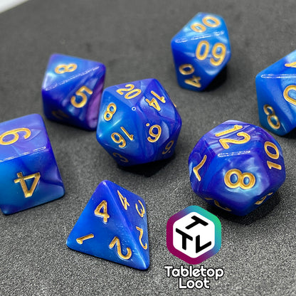 A close up of the Mystique 7 piece dice set from Tabletop Loot with swirls of purple in pearlescent blue and gold numbering.
