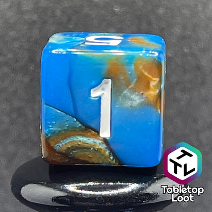 A close up of the D6 from the Patina Copper 7 piece dice set from Tabletop Loot with swirls of pearlescent blue and orange and white numbering.