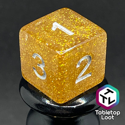A close up of the D6 from the Pixie Dust 7 piece dice set from Tabletop Loot; gold glittery dice with silver numbering.