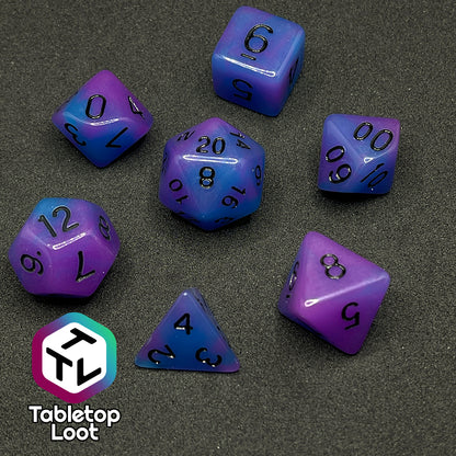 The Quantum 7 piece dice set from Tabletop Loot with swirls of blue and purple glow pigment and black numbering, shown in light.