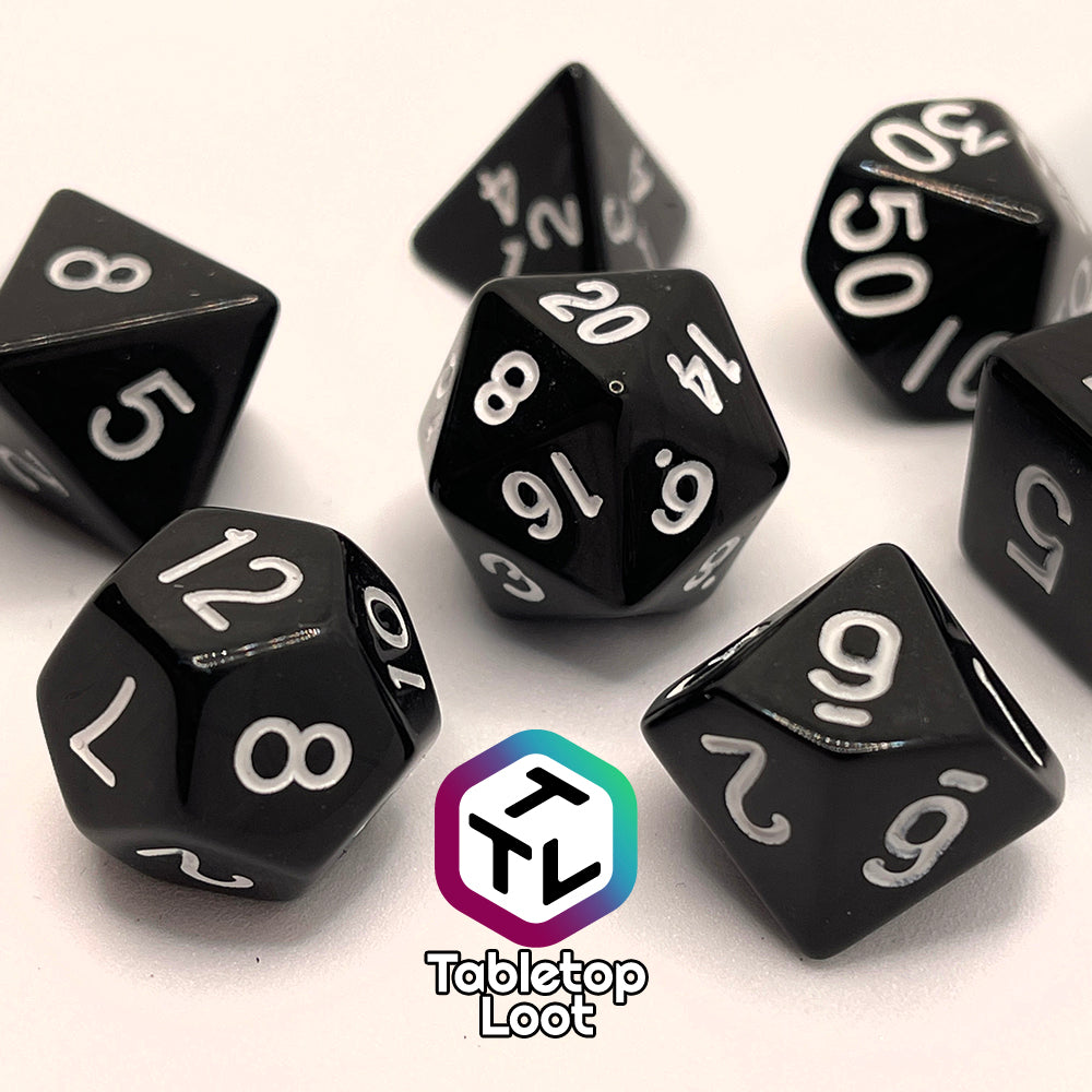 A close up of the Ravenous Void 7 piece dice set; solid black with white numbering.