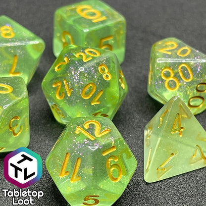 A close up of the Sprites 7 piece dice set from Tabletop Loot with light green translucent pigment packed with glitter and gold numbering.