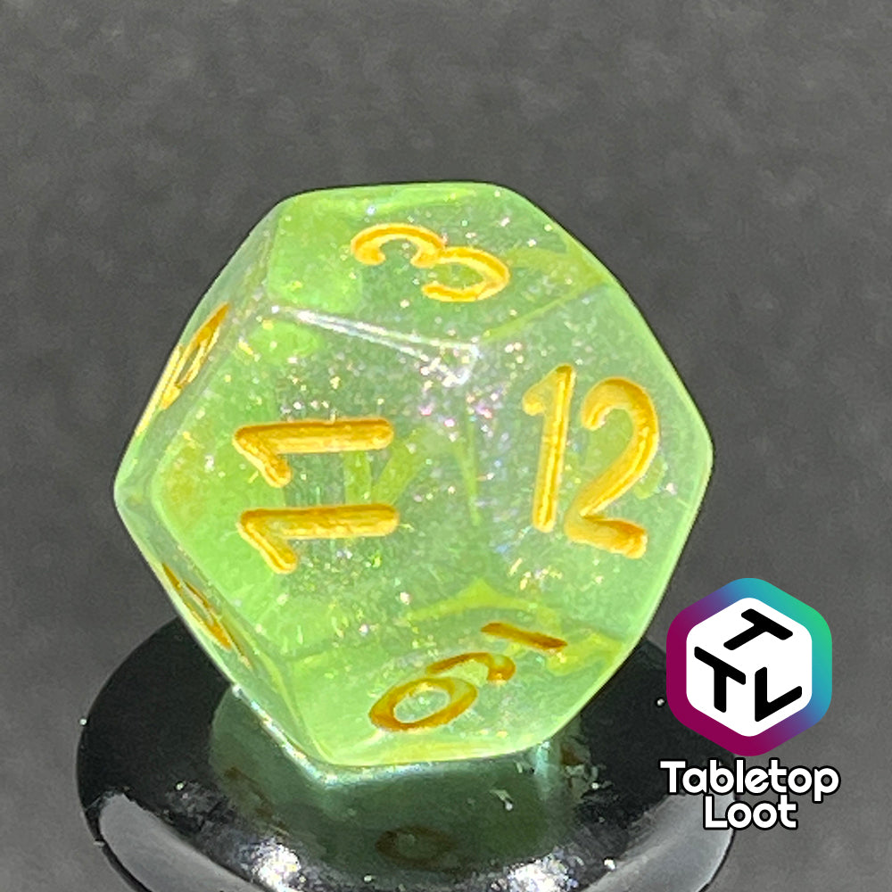 A close up of the D12 from the Sprites 7 piece dice set from Tabletop Loot with light green translucent pigment packed with glitter and gold numbering.