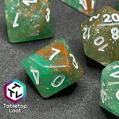 A close up of the D10 from the Star Hatchery 7 piece dice set from Tabletop Loot with swirls of orange and green suspended in glittery clear resin with white numbers.