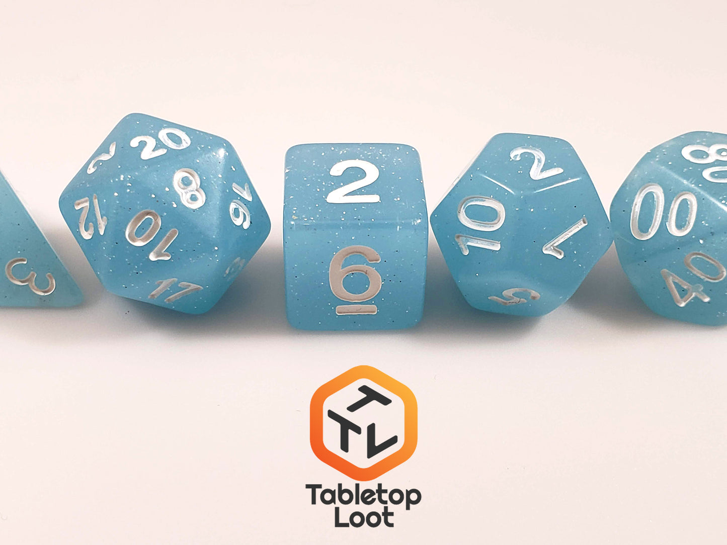 The Frosted Blueberry 7 piece dice set from Tabletop Loot with light blue sparkly resin and silver numbering.