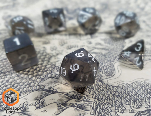 A close up of the D20 from the Shadow Thrall 7 piece dice set from Tabletop Loot; grey tinted like smoky quartz with white numbering.