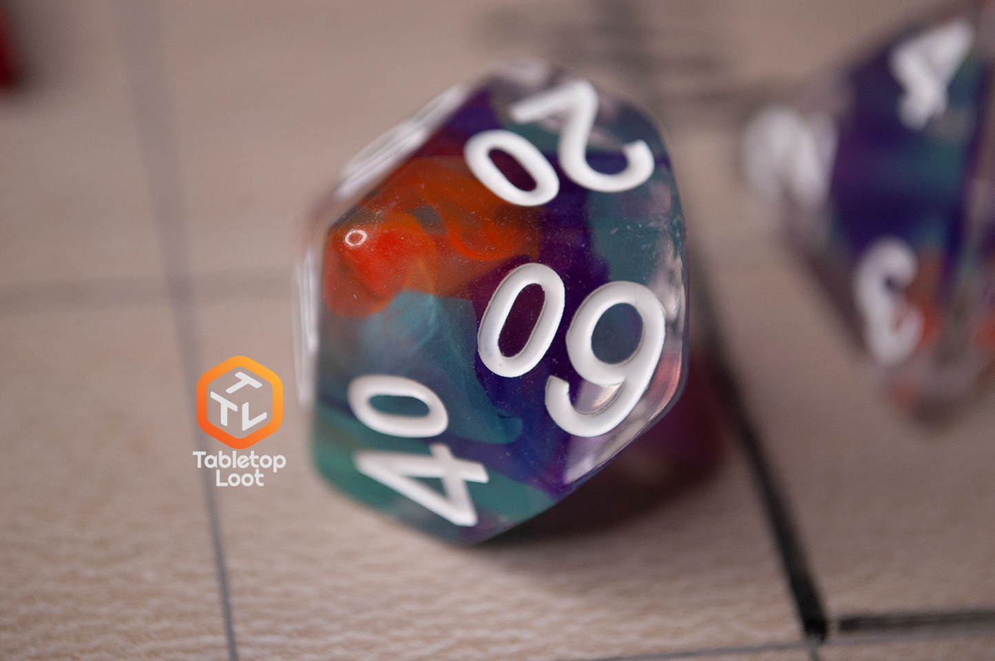 A close up of the Raise the Banners percentile die, clear with swirls of orange, blue, and purple.