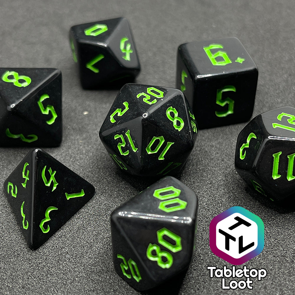 A close up of the Xenomorph 7 piece dice set from Tabletop Loot with bright green bold gothic numbers on highly reflective black dice.