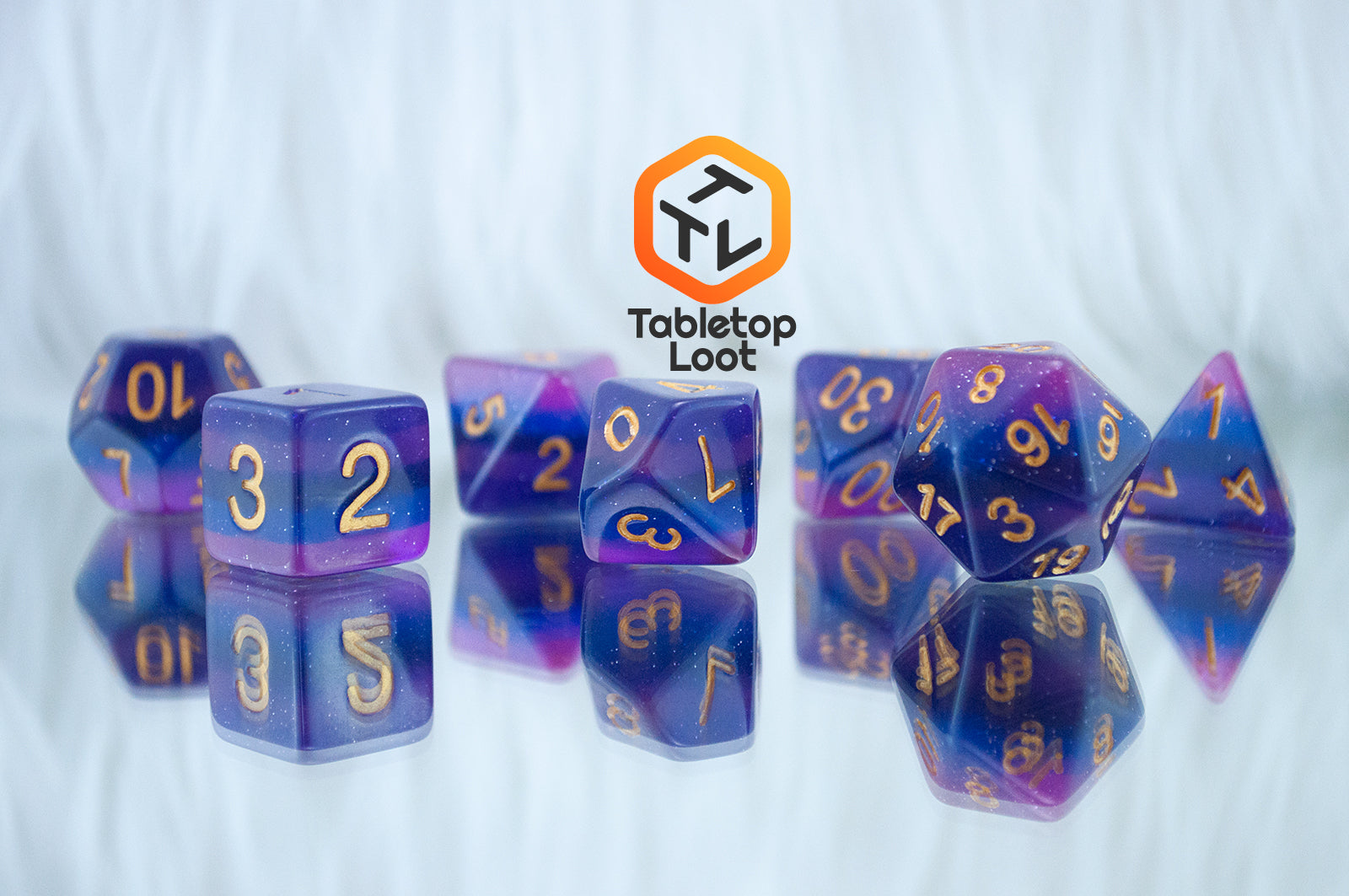 A close up of the Lavender Galaxy 7 piece dice set from Tabletop Loot with layers of pink, purple, and blue, lots of glitter, and gold numbering.