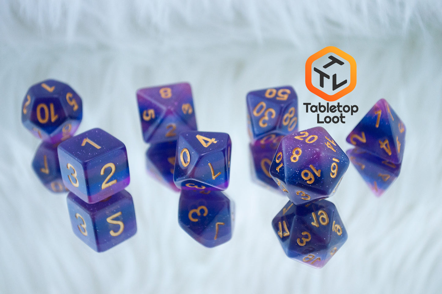 The Lavender Galaxy 7 piece dice set from Tabletop Loot with layers of pink, purple, and blue, lots of glitter, and gold numbering.