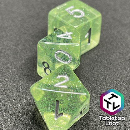 A close up of the D8, D10, and D6 from the Acid Splash 7 piece dice set from Tabletop Loot; glittery lime green translucent dice with silver numbering.