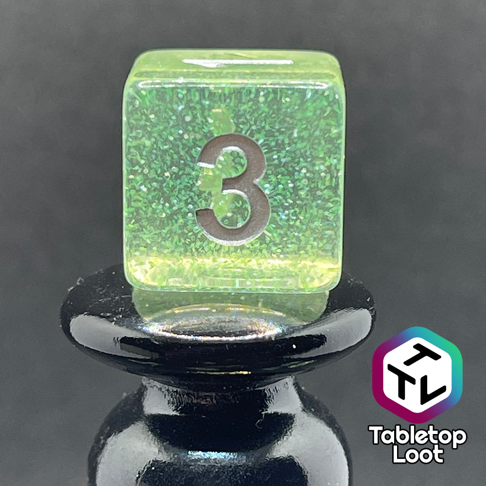 A close up of the D6 from the Acid Splash 7 piece dice set from Tabletop Loot; glittery lime green translucent dice with silver numbering.