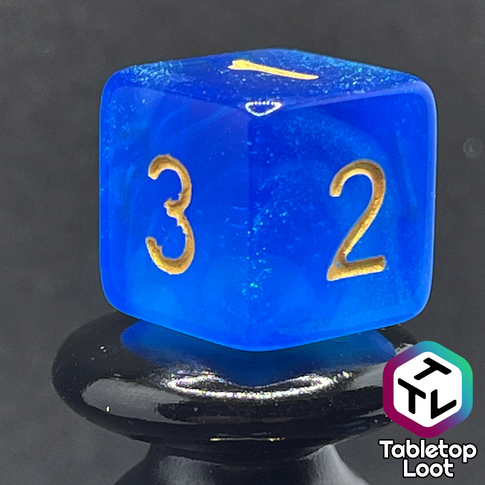 A close up of the D6 from the Air Genasi 7 piece dice set from Tabletop Loot with swirls of glittering tones of blue and gold numbers.