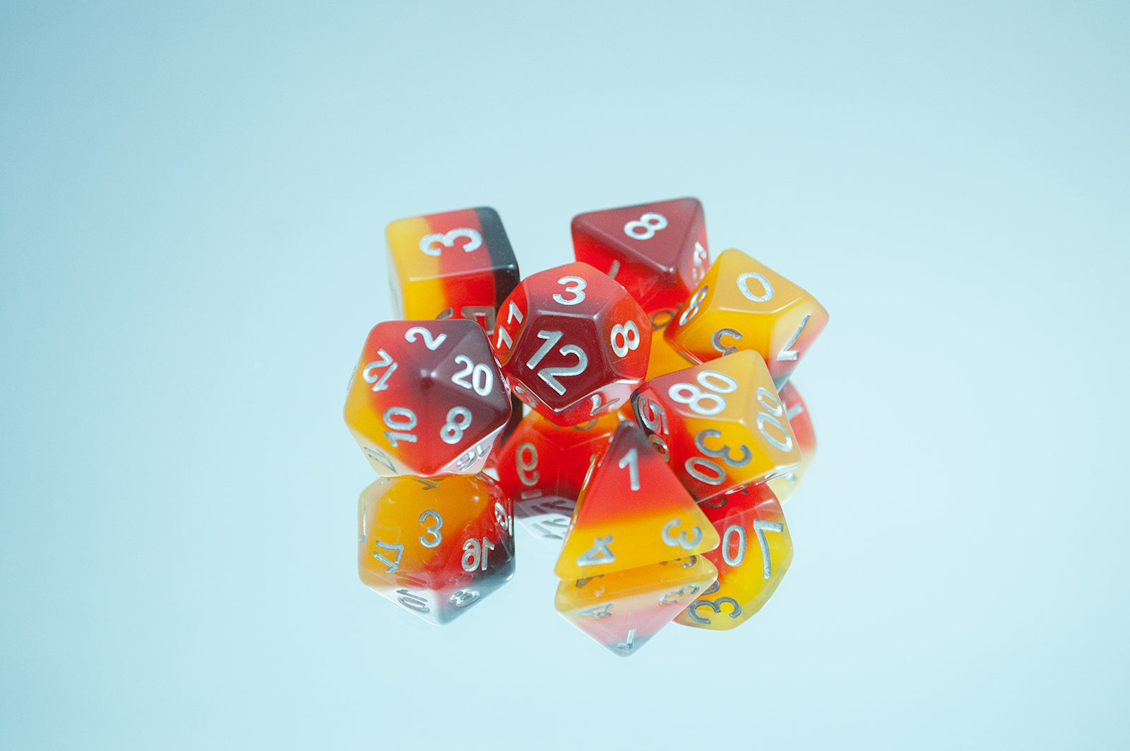 The Amber 7 piece dice set from Tabletop Loot with layers of black, red, orange, and yellow resin and silver numbering.
