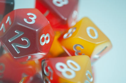 A close up of the Amber 7 piece dice set from Tabletop Loot with layers of black, red, orange, and yellow resin and silver numbering.