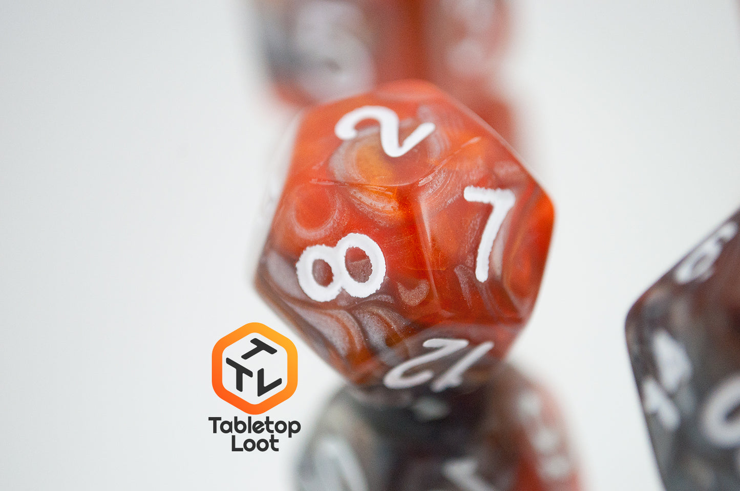 A close up of the D12 from the Amber Shard 7 piece dice set from Tabletop Loot with swirls of orange and silver resin and white numbers.