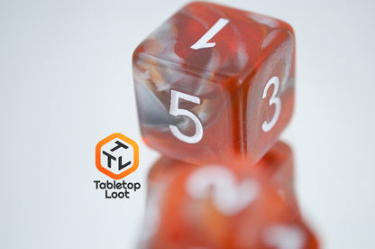 A close up of the D6 from the Amber Shard 7 piece dice set from Tabletop Loot with swirls of orange and silver resin and white numbers.