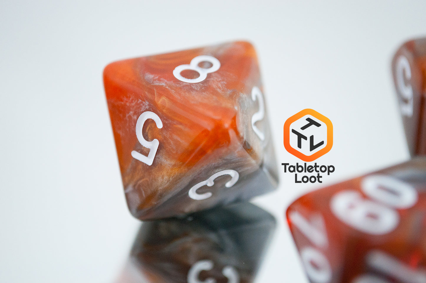 A close up of the D8 from the Amber Shard 7 piece dice set from Tabletop Loot with swirls of orange and silver resin and white numbers.