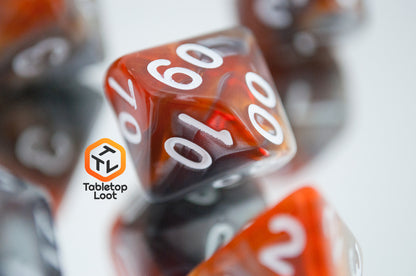 A close up of the percentile die from the Amber Shard 7 piece dice set from Tabletop Loot with swirls of orange and silver resin and white numbers.