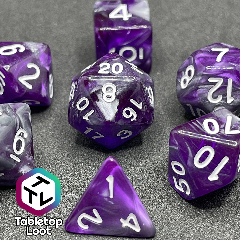A close up of the Amethyst Dreams 7 piece dice set with swirls of purple and silver and white numbering.
