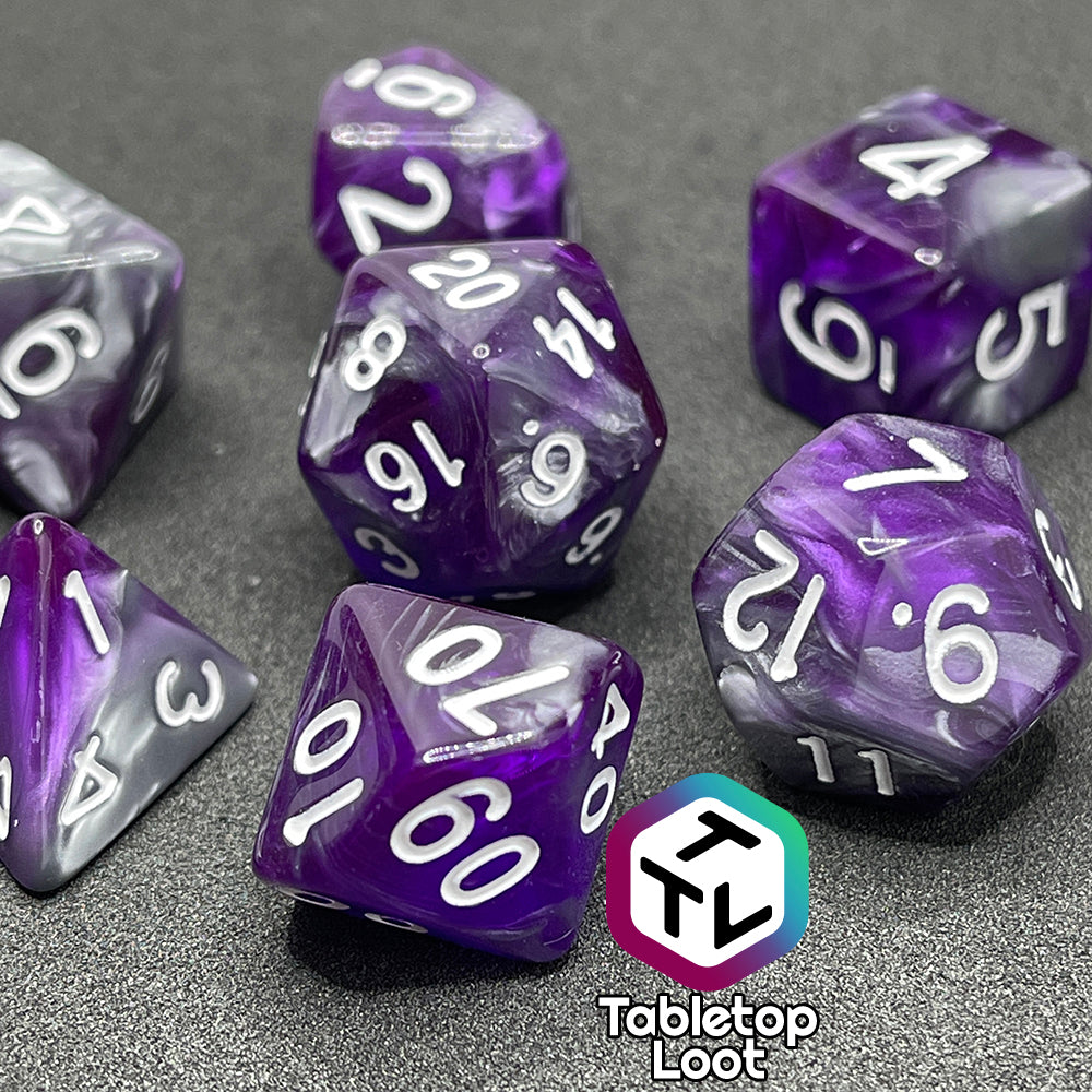 A close up of the Amethyst Dreams 7 piece dice set with swirls of purple and silver and white numbering.