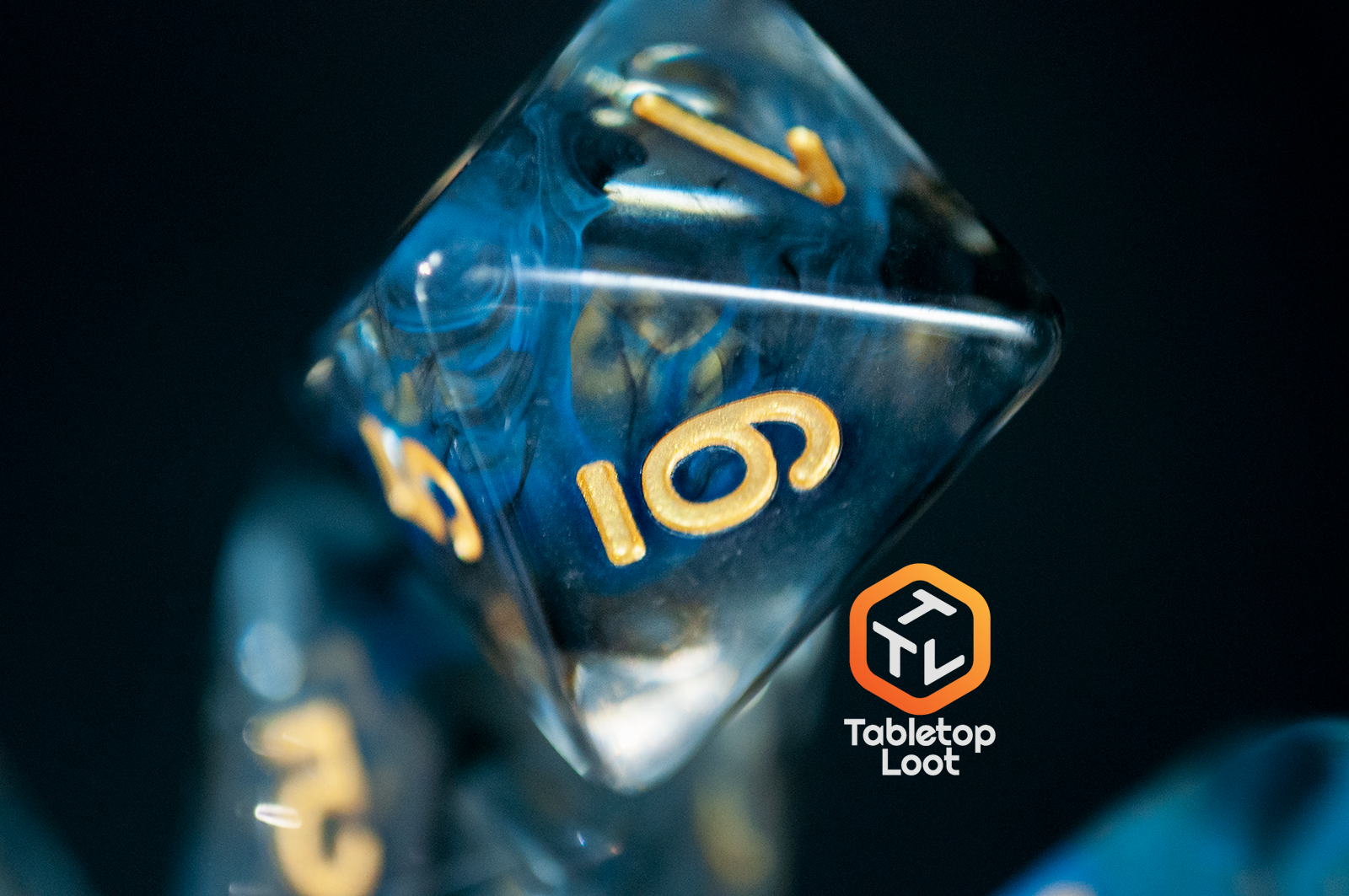A close up of the D8 from the Arcane Eye 7 piece dice set from Tabletop Loot with swirls of blue and black in clear dice and gold numbering.