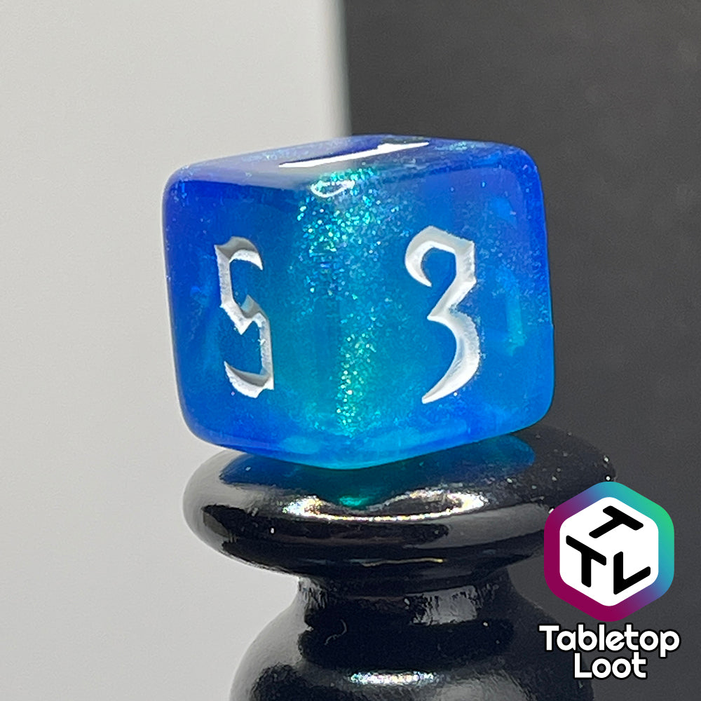 A close up of the D6 from the Armor of Agathys 7 piece dice set from Tabletop Loot with shimmering tones of blue swirling together and white numbering in a gothic font.