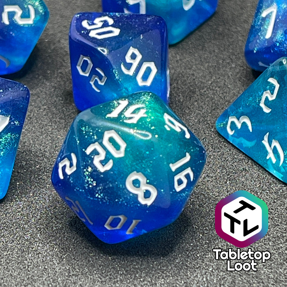 A close up of the D20 from the Armor of Agathys 7 piece dice set from Tabletop Loot with shimmering tones of blue swirling together and white numbering in a gothic font.