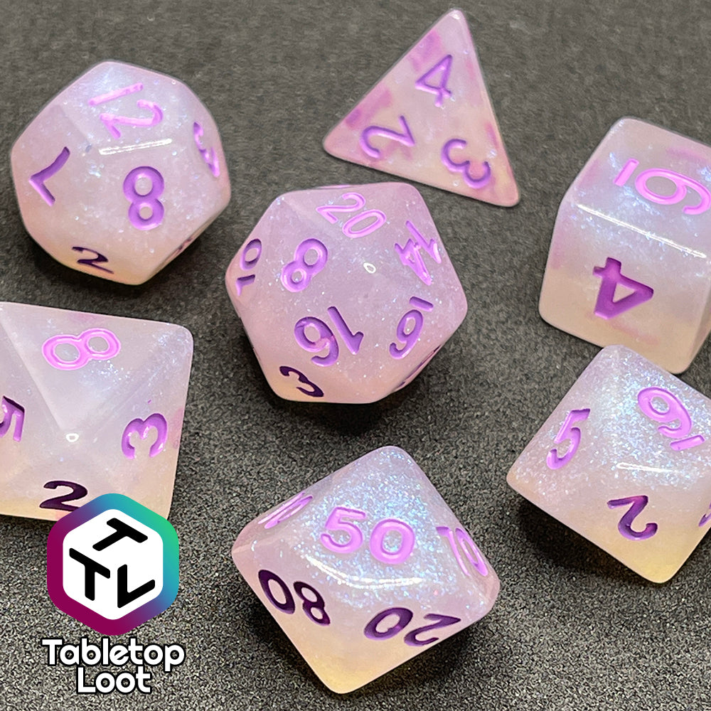 A close up of the Astral Projection 7 piece dice set from Tabletop Loot with lavender numbering on milky dice with iridescent shimmer.