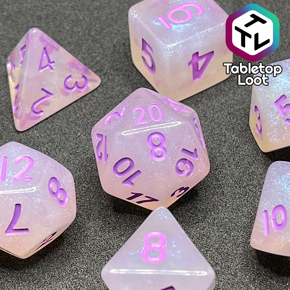 A close up of the Astral Projection 7 piece dice set from Tabletop Loot with lavender numbering on milky dice with iridescent shimmer.