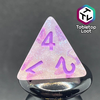 A close up of the D4 from the Astral Projection 7 piece dice set from Tabletop Loot with lavender numbering on milky dice with iridescent shimmer.