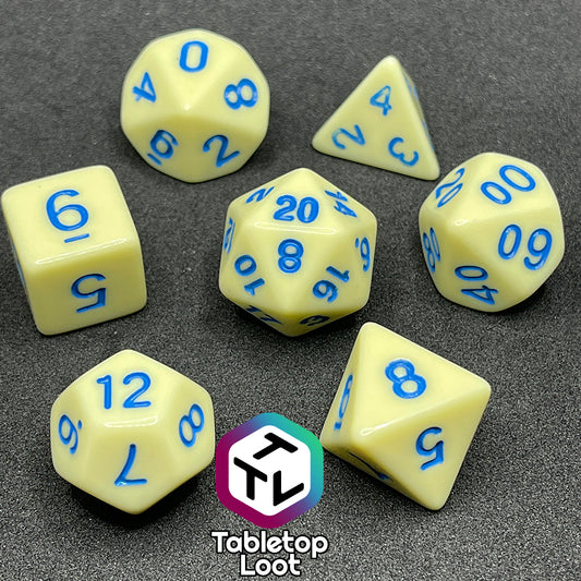 The Belle 7 piece dice set from Tabletop Loot with cornflower blue numbering on solid pastel yellow faces.
