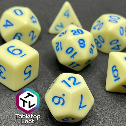A close up of the Belle 7 piece dice set from Tabletop Loot with cornflower blue numbering on solid pastel yellow faces.