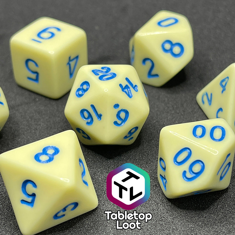 A close up of the Belle 7 piece dice set from Tabletop Loot with cornflower blue numbering on solid pastel yellow faces.
