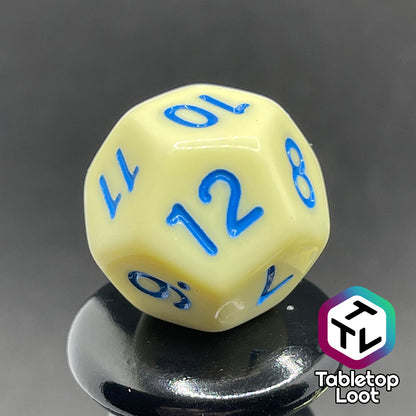 A close up of the D12 from the Belle 7 piece dice set from Tabletop Loot with cornflower blue numbering on solid pastel yellow faces.