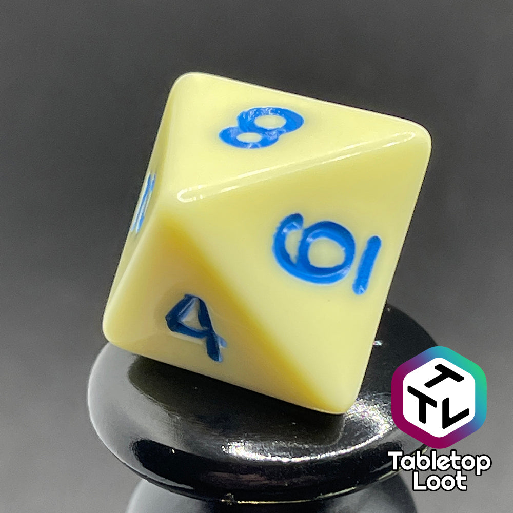 A close up of the D8 from the Belle 7 piece dice set from Tabletop Loot with cornflower blue numbering on solid pastel yellow faces.