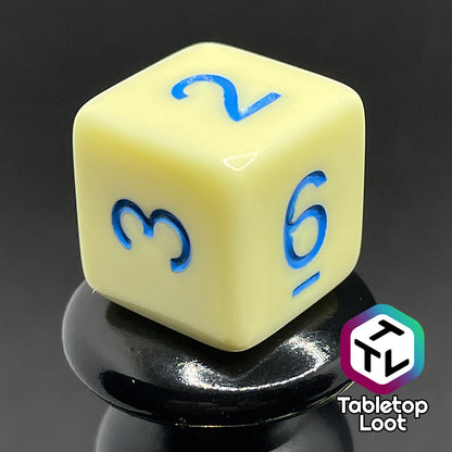 A close up of the D6 from the Belle 7 piece dice set from Tabletop Loot with cornflower blue numbering on solid pastel yellow faces.