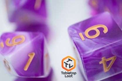 A close up of the Berry Blast 7 piece dice set from Tabletop Loot with swirls of purple and white and gold numbering.