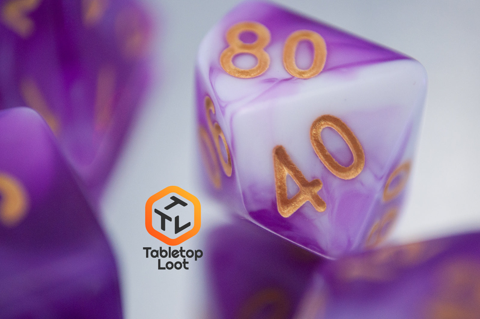 A close up of the percentile die from the Berry Blast 7 piece dice set from Tabletop Loot with swirls of purple and white and gold numbering.