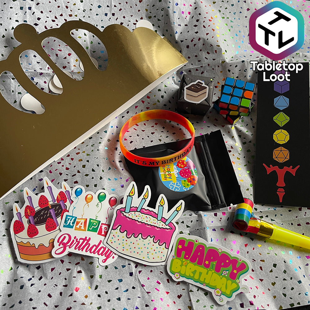 A gold foil paper crown next to a silicone bracelet, puzzle cube, bookmark, noise maker, and several birthday themed stickers.