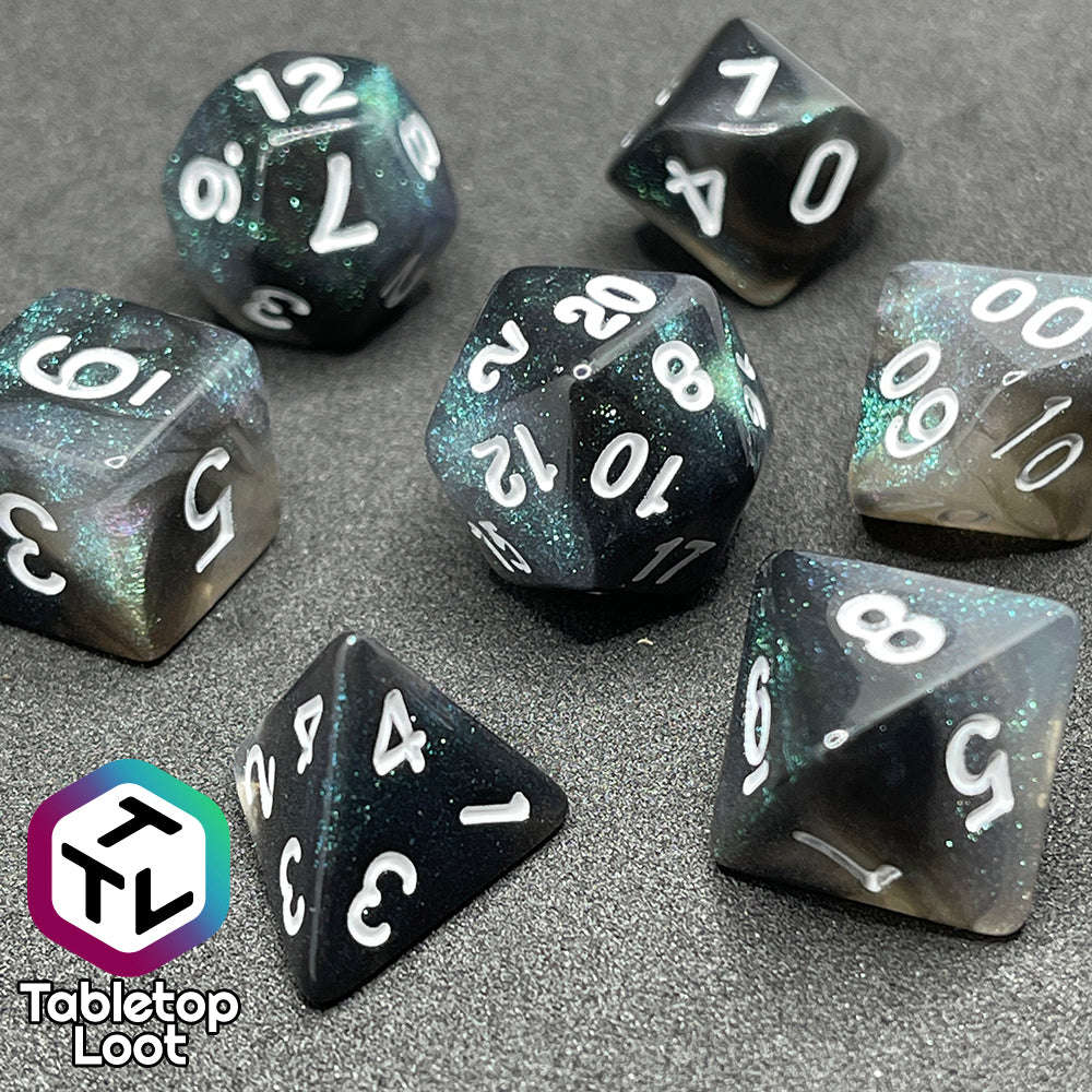 A close up of the Black Moonstone 7 piece dice set from Tabletop Loot with swirls of black and teal iridescent glitter, inked in white.