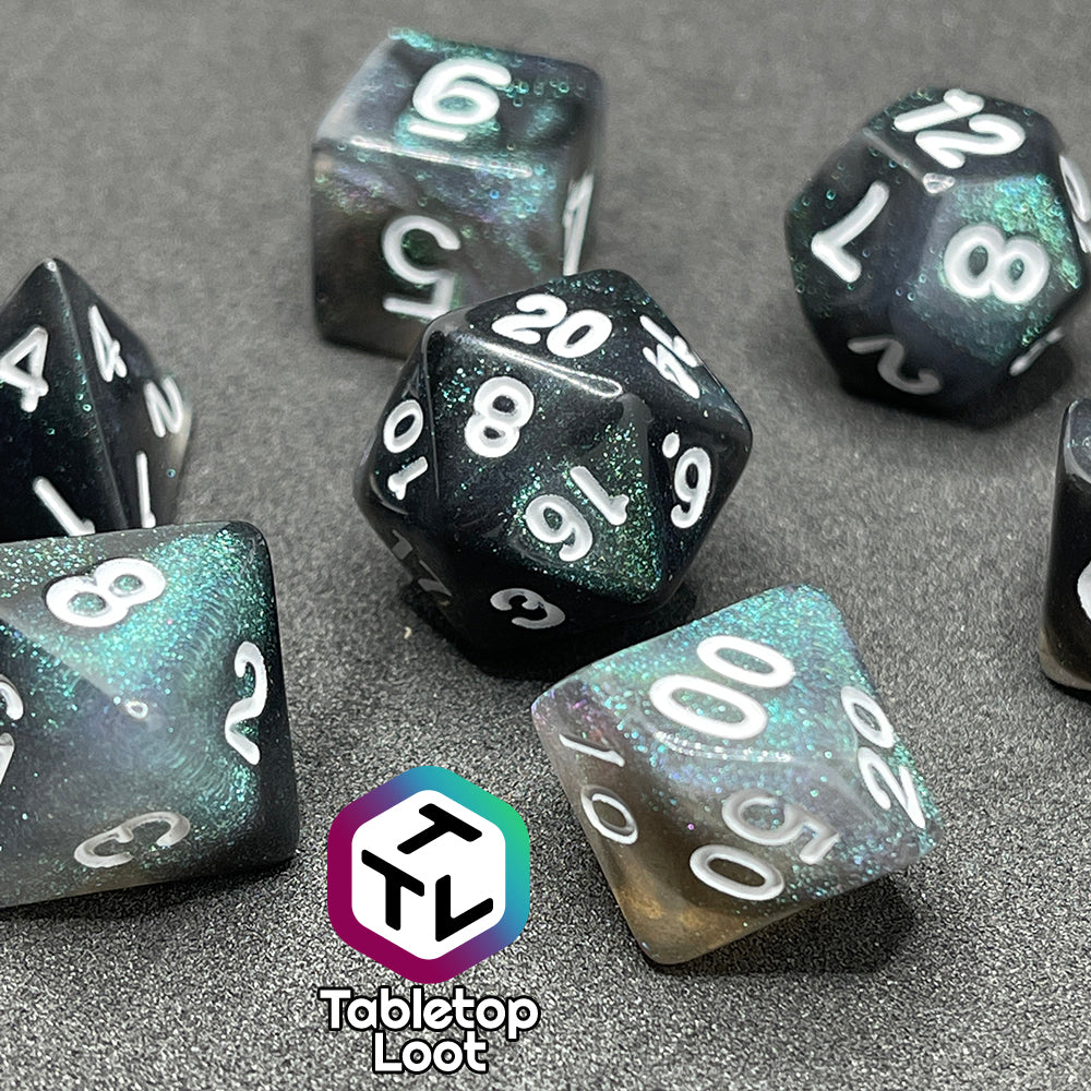 The Black Moonstone 7 piece dice set from Tabletop Loot with swirls of black and teal iridescent glitter, inked in white.