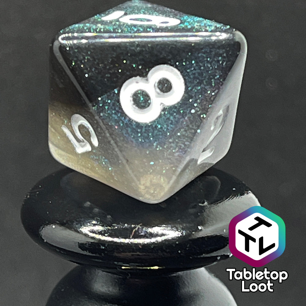 A close up of the D8 from the Black Moonstone 7 piece dice set from Tabletop Loot with swirls of black and teal iridescent glitter, inked in white.